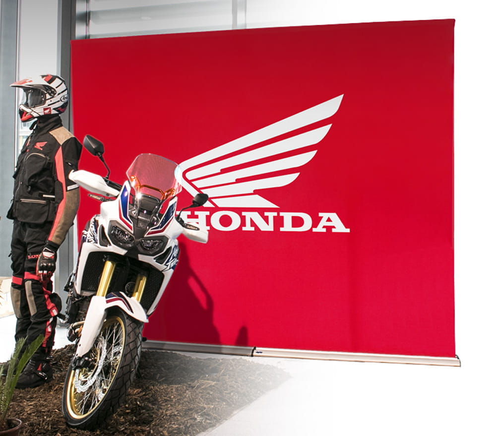 Einsatzbeispiel Easywall Flex Honda Einsatzbeispiel des Produkts 'Easywall Flex' mit einem roten Hintergrund und dem Honda-Logo, daneben ein Motorrad und ein Fahrer in Schutzkleidung.
