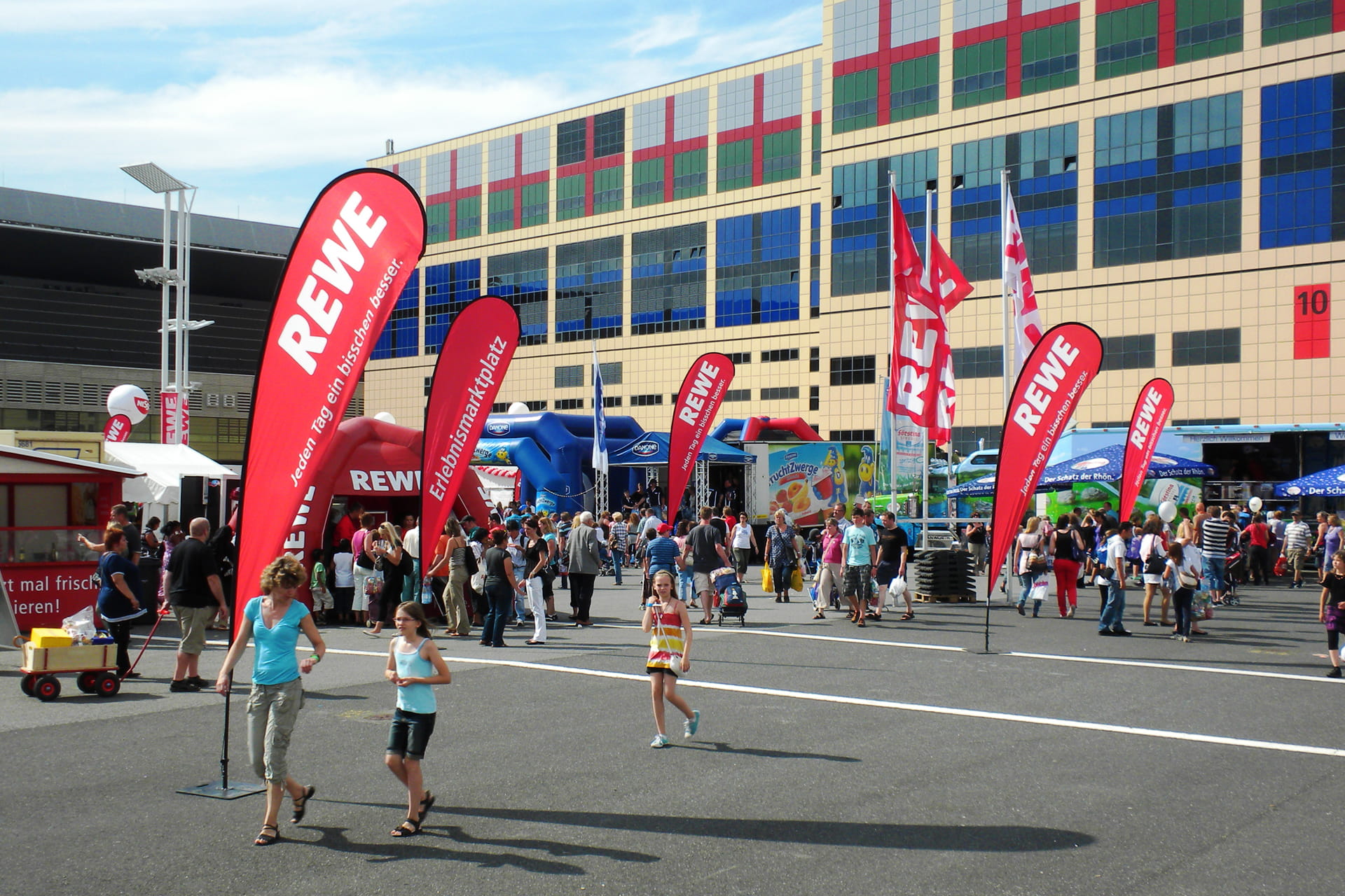 Event vor einer Messerhalle mit Fahnen und Zelten im Design des Rewe-Supermarktes