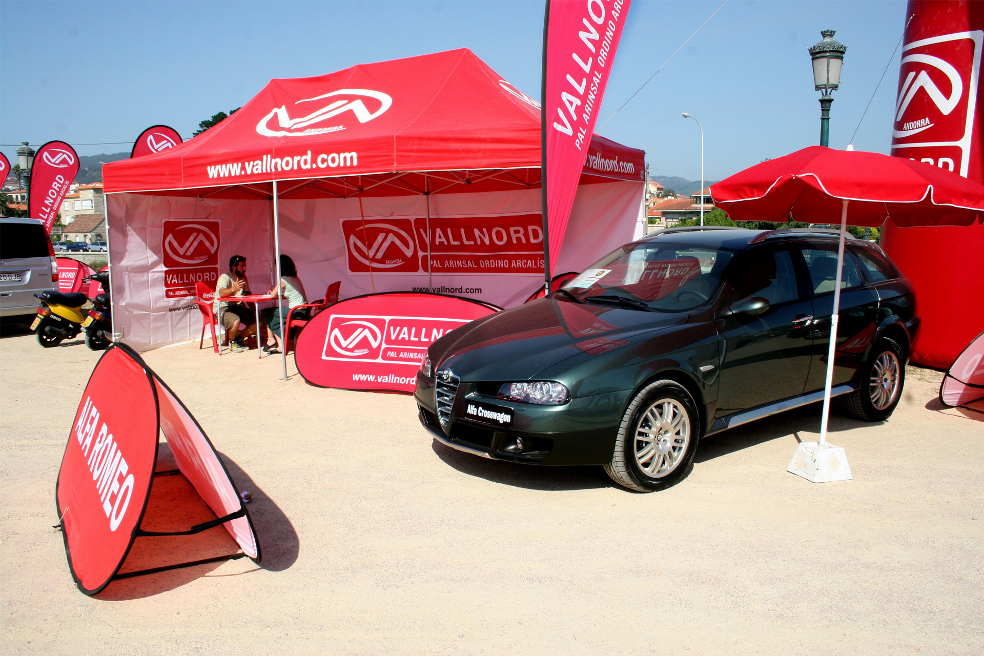 Ein Auto park vor einem Eventzelt mit Logodruck in rot, mit Schirm und Fahnen