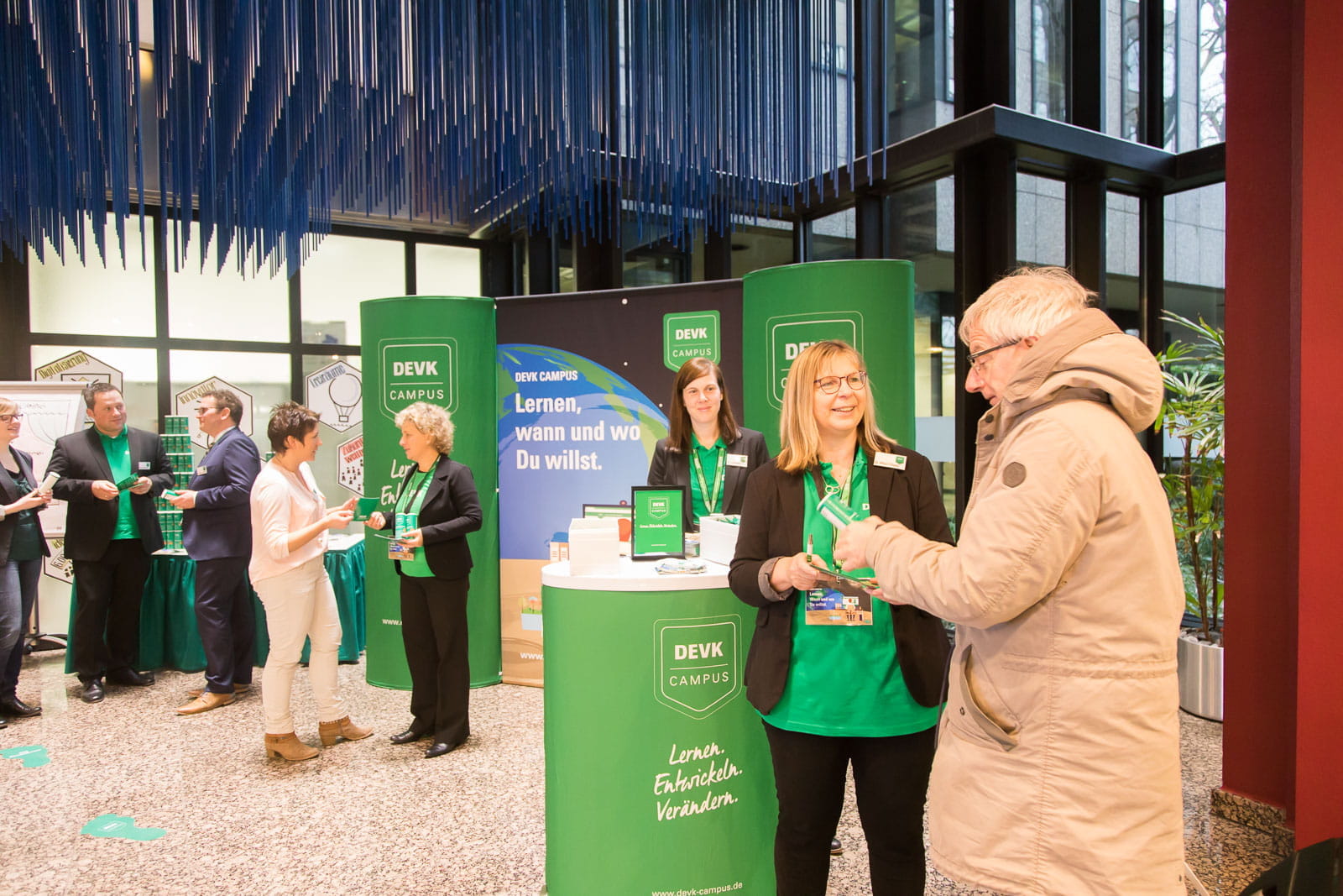 Messesystem Messewand Easy360 Messe DEVK Messesystem mit DEVK-Logo, Mitarbeiter in grünen Shirts, Besucher im Gespräch, Messeumgebung.