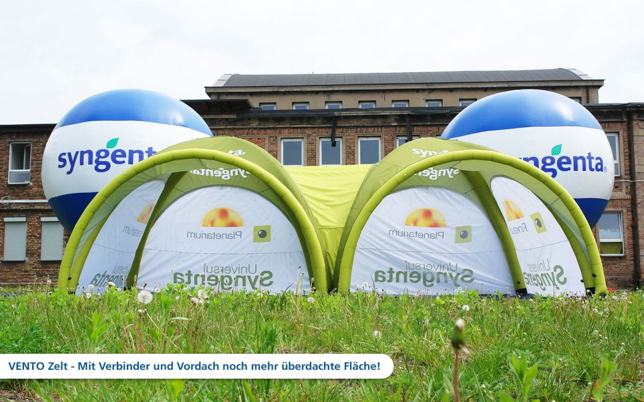 Vento Aufblasbares Zelt von Syngenta Aufblasbares Zelt 'Vento' von Syngenta mit zwei großen, blauen Ballons und grüner Überdachung auf einer Wiese.