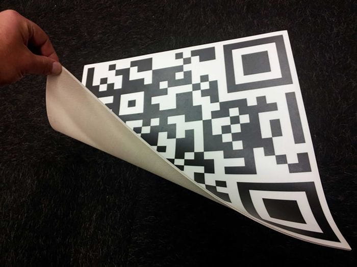 Einsatzbeispiel Fußbodenbelag mit QR Code Motiv Fußbodenbelag mit QR-Code-Motiv, teilweise umgeklappt, zeigt den QR-Code und die Unterseite des Belags.