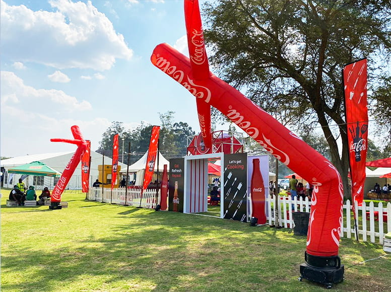 Aufblasbare Werbung Coke Slider Aufblasbare Werbung in Form von roten, tanzenden Figuren mit Coca-Cola Branding auf einem Eventgelände.