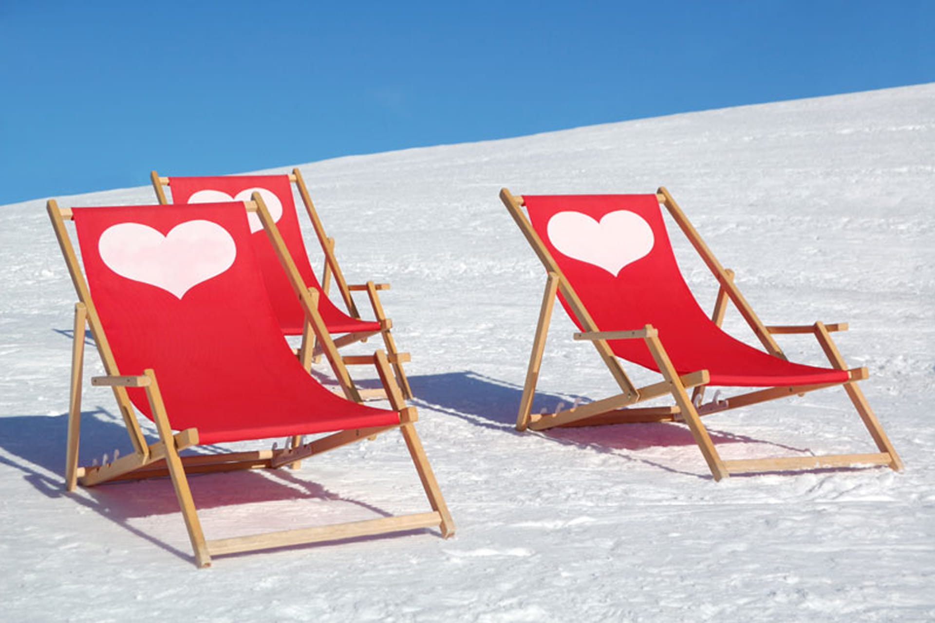 Drei rote Liegestühle auf einer Schneefläche mit weißen Herzen auf der Liegefläche