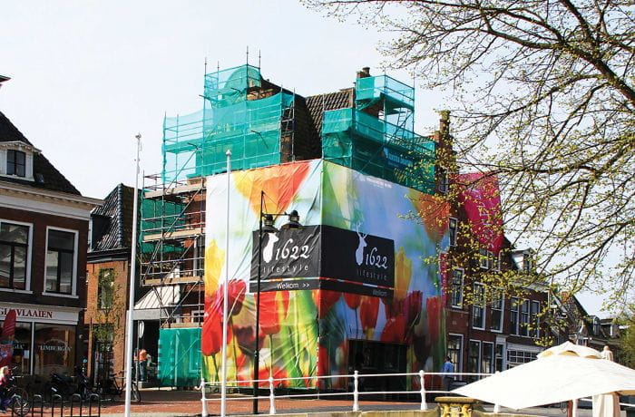 Gerüstbanner Haus Gerüstbanner mit buntem Design an einem renovierten Gebäude, umgeben von Gerüsten.