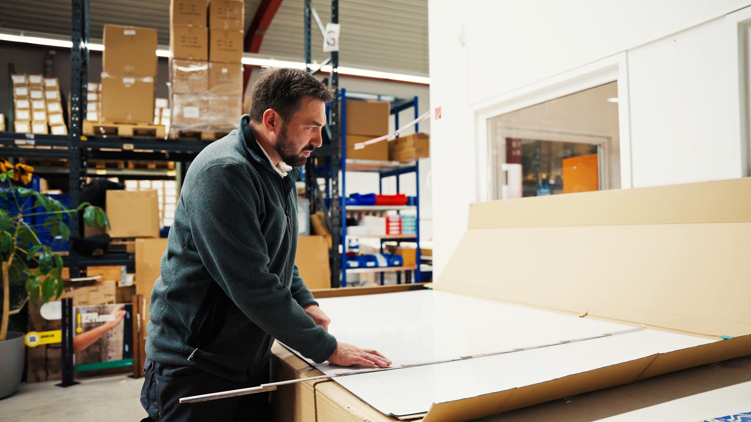 Mann in einem Lagerraum, der eine große Verpackung öffnet, um Produkte auszupacken.