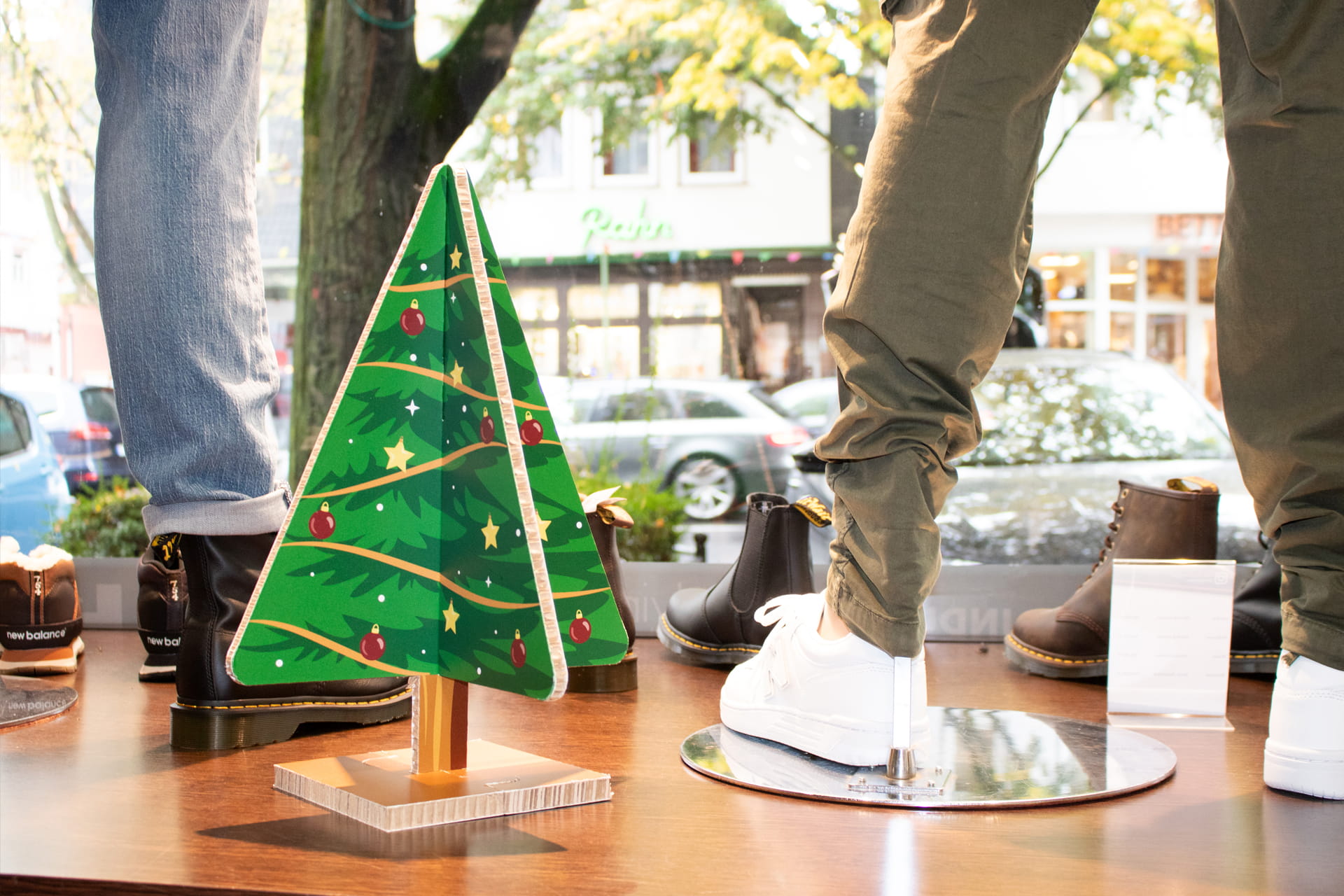 Giveaway-Weihnachtsbaum aus Reboard Zusammensteckbarer Weihnachtsbaum aus Wabenkarton auf einem Podest neben Schaufensterpuppen