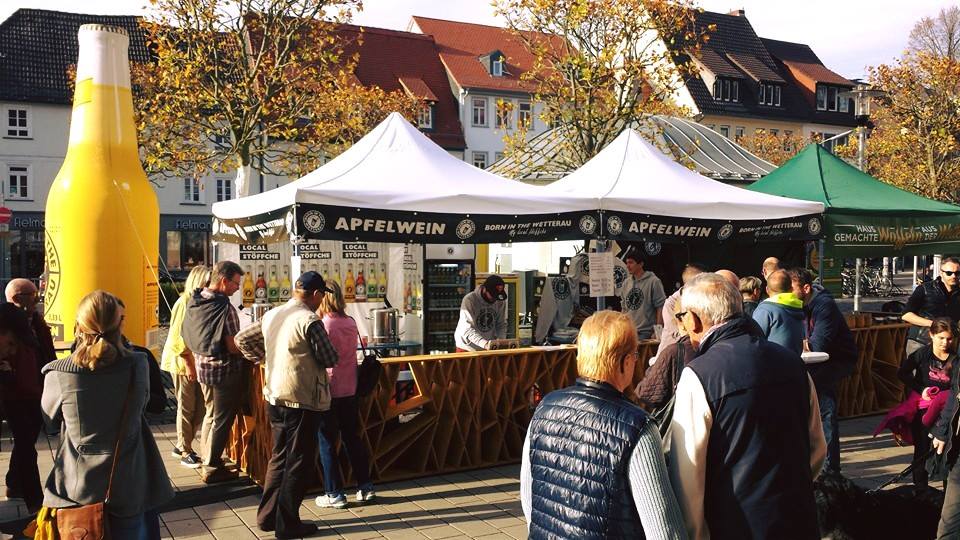 Born In The Wetterau Markt Evenzelt Easydome Aufblasbare Flasche Easy Inflate Ad Marktstand mit aufblasbarer Flasche und Menschenmenge, die Apfelwein probiert.