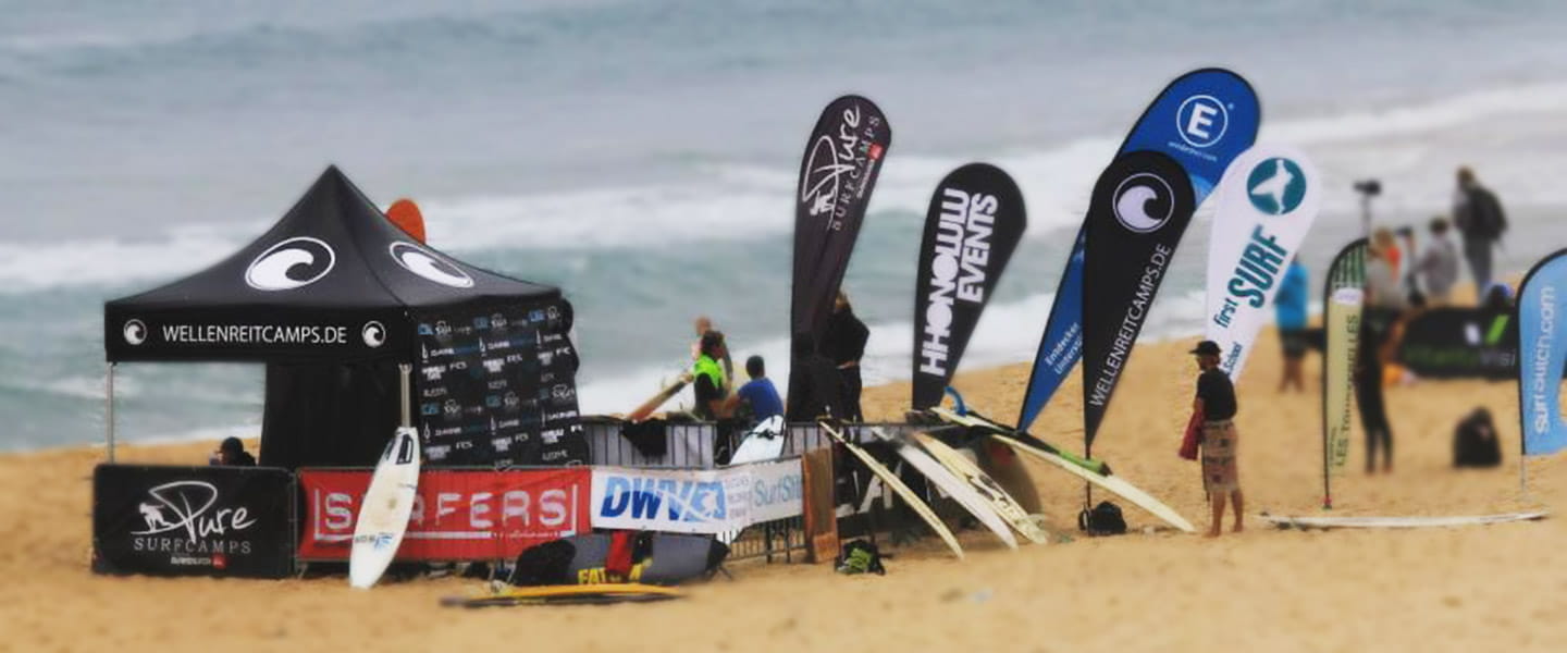 Einsatzbeispiel Easyflag Wellenreitcamp Zelt und Beachflags am Strand für das Wellenreitcamp, mit Surfboards und Teilnehmern im Hintergrund.